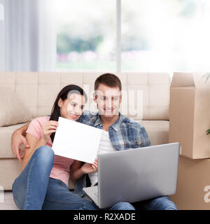 Beautiful young couple using laptop communicates via Skype. Woman smiles and shows blank sheet of paper. Stock Photo