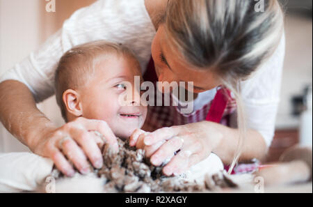 A happy handicapped down syndrome child with his mother indoors baking. Stock Photo