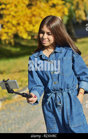 Young beautiful girl in denim suit takes selfie walking in city Park in autumn Stock Photo