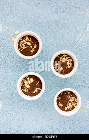 Homemade chocolate pudding in four white ceramic ramekins, decorated with roasted almond slivers, on light blue concrete background with copy space. T Stock Photo