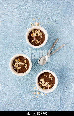 Homemade chocolate pudding in three white ceramic ramekins and teaspoons on light blue concrete background with copy space. Top view. Stock Photo