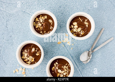 Homemade chocolate pudding in three white ceramic ramekins with roasted almond slivers and teaspoons on light blue concrete background. Top view. Stock Photo
