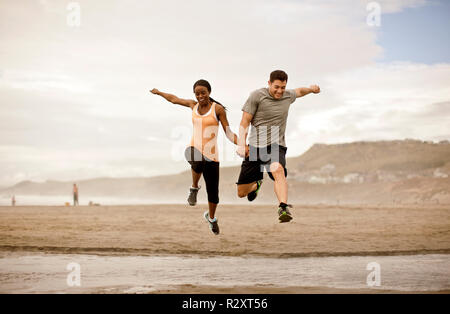 Smiling young couple jumping over shallow water on a beach. Stock Photo