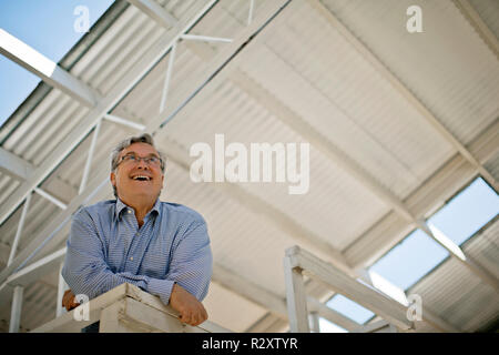 Mature man grinning while leaning on the railing of a balcony. Stock Photo