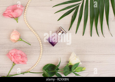 Bottle of perfume, beads on a string with white and pink flowers and green leaves on wooden background. Woomen cosmetics. Top view. Stock Photo