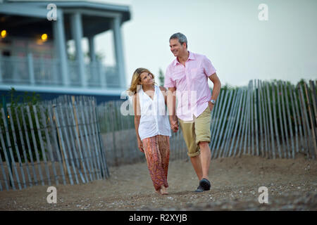 Mature couple holding hands and smiling as they walk on the beach at sunset. Stock Photo