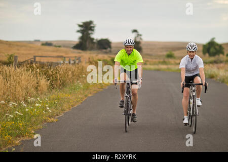 Portrait of a happy mature couple cycling along a country road. Stock Photo