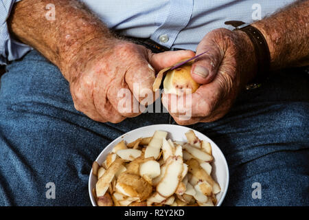 A man seated using a sharp knife to peel potatoes. Stock Photo