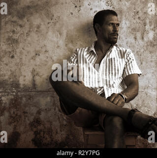 Side view of a man sitting on a wooden stool. Stock Photo