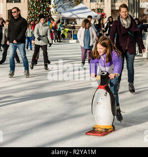 Reston VA -- November 17, 2018. The Reston Town Center rink is full of ice skaters; a young girl skates down the ice using a toy Penguin to help balan Stock Photo