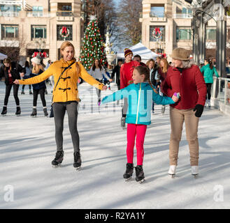 Reston VA -- November 17, 2018. The Reston Town Center rink is full of ice skaters; two women help a young girl learn how to balance. Stock Photo