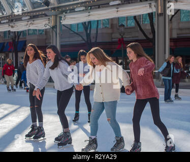 Reson, VA--November 17, 2018. Four young women are ice skating in the Reston Town Center rink; two are helping a friend to balance. Stock Photo