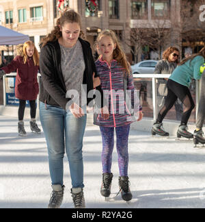 Reston VA -- November 17, 2018. A young woman and girl are ice skating together on the Reston Town Center rink; the young woman is helping the younger Stock Photo