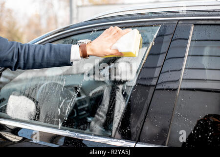 Businessman washing car window with sponge and foam on a self service car wash, close-up view with reflection on the window Stock Photo