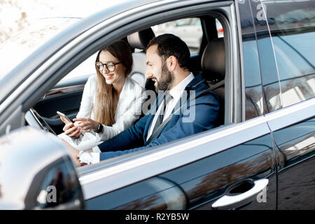 Businessman and woman dressed in the suits talking together while driving a luxury car in the city Stock Photo