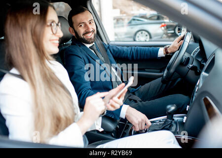 Businessman and woman dressed in the suits talking together while driving a luxury car in the city Stock Photo