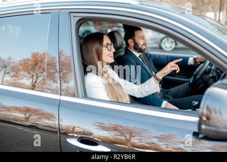 Businessman and woman dressed in the suits driving luxury car, view from the outside through the window Stock Photo