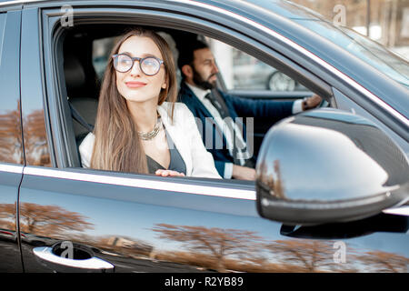 Elegant businesswoman looking out the window driving luxury car with businessman in the city Stock Photo