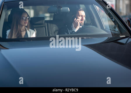 Businessman talking with phone while driving a luxury car with woman, view from the outside through the windshield Stock Photo