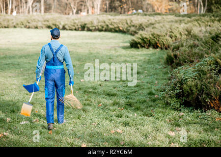 Professional sweeper or gardener in working uniform walking with cleaning tools in the garden Stock Photo