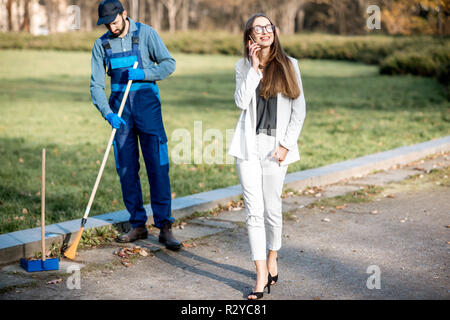 Elegant businesswoman walking through the man sweeping the street with arrogant attitude. Poverty and wealth concept Stock Photo