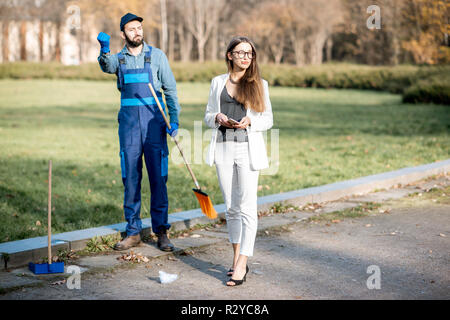 Businesswoman threw garbage with arrogant attitude near the man sweeping the street. Poverty and wealth concept Stock Photo