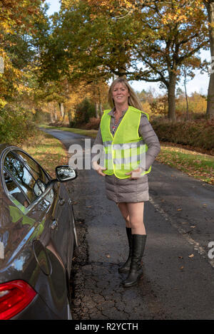 Woman motorist by her car putting on a reflective safety jacket Stock Photo