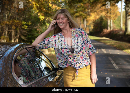 Woman motorist leaning on her car using a mobile telephone Stock Photo