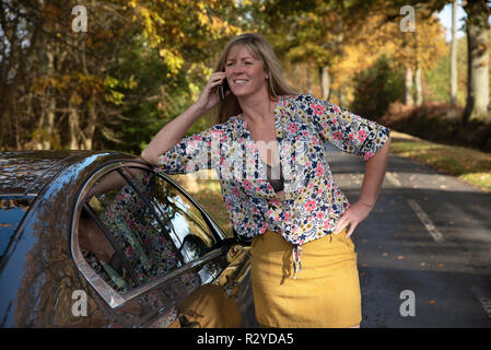 Woman motorist leaning on her car using a mobile telephone Stock Photo