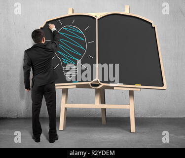 Businessman drawing lamp on book shape blackboard Stock Photo