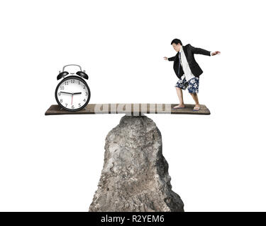Man balancing against alarm clock at hilltop isolated in white background Stock Photo