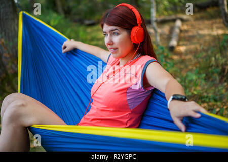 Photo of brunette in headphones listening to music while sitting in hammock on forest background Stock Photo