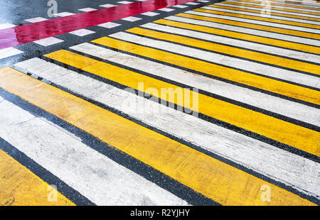 Pedestrian crossing with white, yellow and red stripes on wet asphalt Stock Photo
