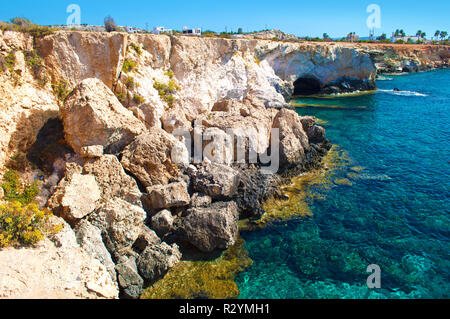 View on a cave near Agia Napa, Cyprus, majestic natural landmark. Yellow brown high stone cliffs near transparent amazing blue water and flowers. Warm Stock Photo