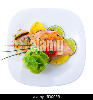 Top view of baked trout fillet served on white plate with potato, grilled onion rings, lime slices and greens. Isolated over white background Stock Photo