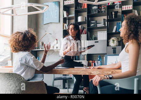 three young women of creative team working indoor using tablet and smart phone - remote working, business, startupper concept Stock Photo