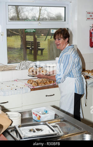 A woman serving hot cross buns in a Uk village hall Stock Photo