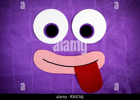 Funny face with tongue stuck out. Emotional face made from paper. Purple background. Stock Photo