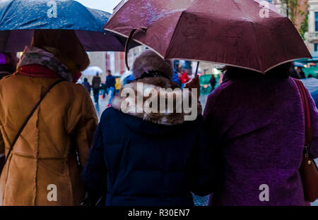 Three women under umbrellas in Gran Via, Madrid, waiting in the rain during a dark late afternoon on Sunday. Stock Photo