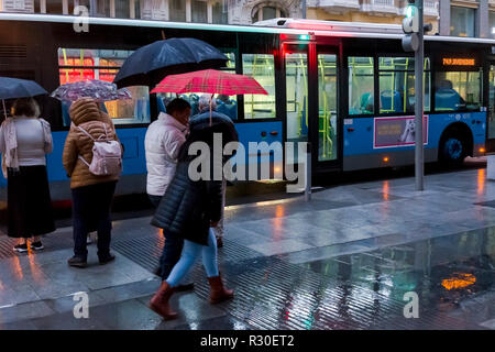 People in Gran Via, Madrid, walking in the rain during a dark late afternoon on Sunday with a bus in the background. Stock Photo