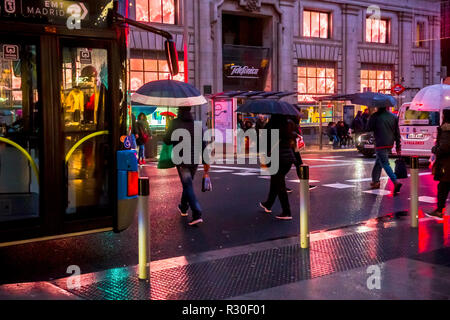 People crossing in Gran Via, Madrid, in the rain during a dark late afternoon on Sunday. Stock Photo