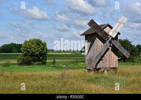 An abandoned wooden windmill in the vast green field near the forest. Barns and other constructions stand next Stock Photo