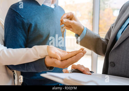 Realtor woman giving house keys to couple, closeup Stock Photo