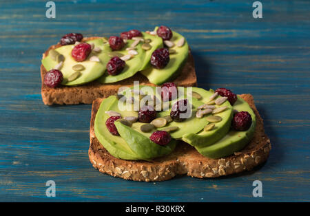 Vegetarian avocado toast with red cranberries and pumpkin seeds and sunflower seeds on a blue wooden background Stock Photo