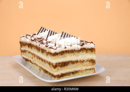 Tiramisu on a rectangular plate on wood table with orange background. Tiramisu is a popular Italian dessert with of layers of sponge cake soaked in co Stock Photo