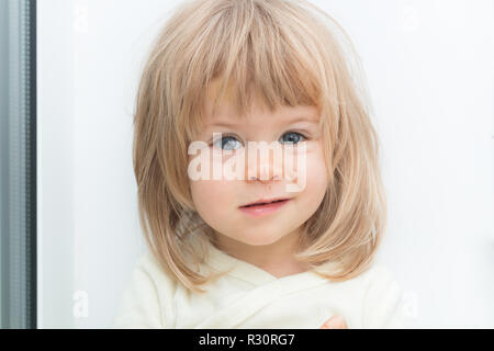 Headshot of adorable cute blonde female child looking at camera with serious upset facial expression. Smirk on face. Pretty little girl with Caucasian traits and scratch on her nose. Attractive baby Stock Photo
