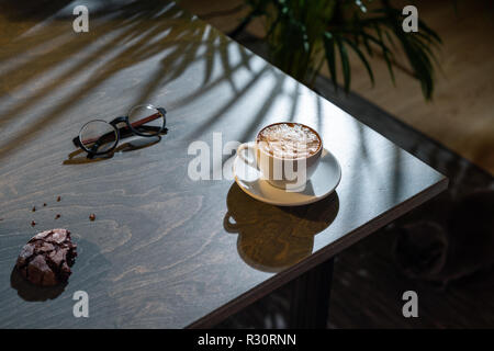 Close up of white coffee cup, oat cookies and glasses on dark wooden table Stock Photo