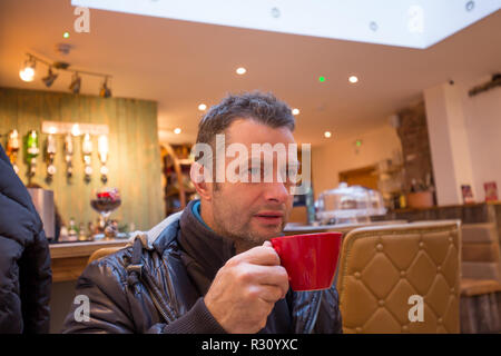 Close up of attractive caucasian male, in his forties, inside trendy bar enjoying a coffee from red cup he is holding. Stock Photo