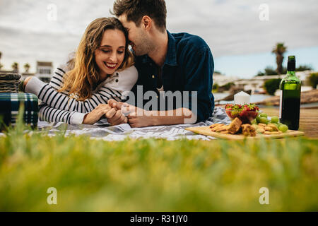 Couple in love on a date enjoying food and drinks sitting outdoors. Smiling man and woman lying down on the ground holding hands and talking while on Stock Photo