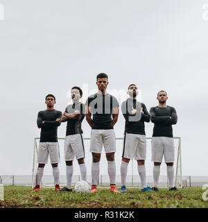 Low angle view of footballers standing on soccer field during practice on a cloudy day. Five footballers standing together with arms crossed on a socc Stock Photo
